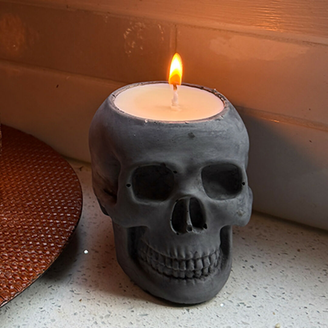 Skull-shaped candle with a lit wick on a textured surface.