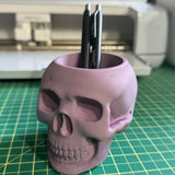 skull shaped candle holder holding pens on a green cutting mat in front of a cutting machine