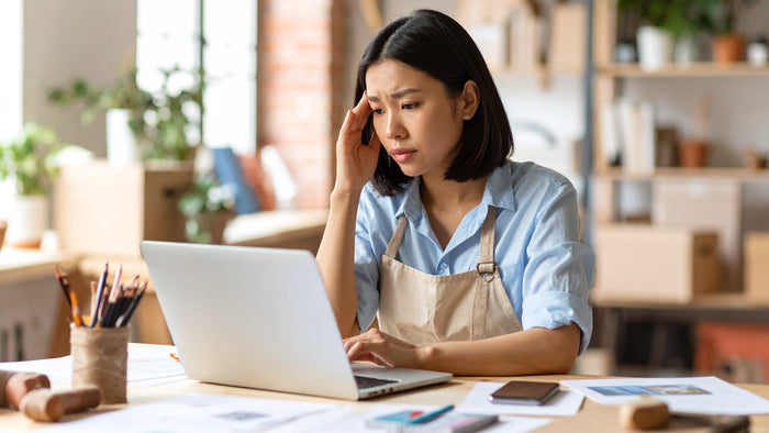 Woman sitting at a desk with a laptop, looking stressed or frustrated.
