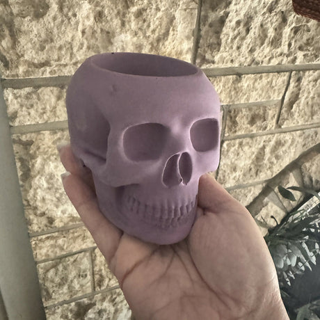 Purple skull-shaped object held in a hand against a textured wall background